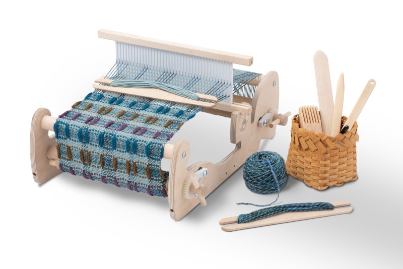 Table top loom with colorful blue green project on the loom and yarn with tools nearby