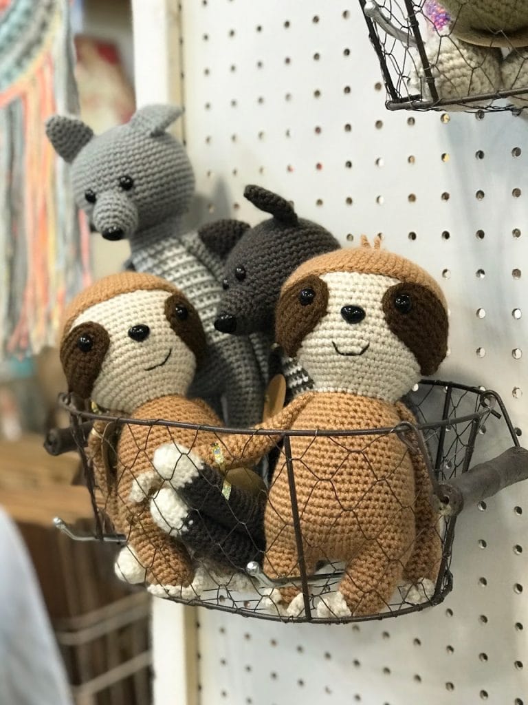 A basket full of crocheted stuffies, namely sloths and wolves, are all smiling from On A Whim Creations.
