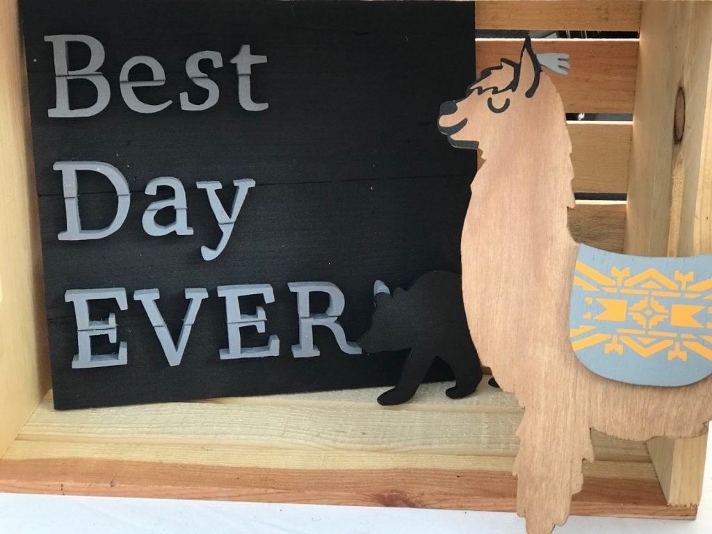 Wood craft booth with a sign that reads "best day ever" and a wooden llama with a decorative blanket design