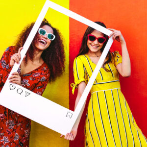 two women stand inside of a large photo frame prop with instagram buttons written on the bottom