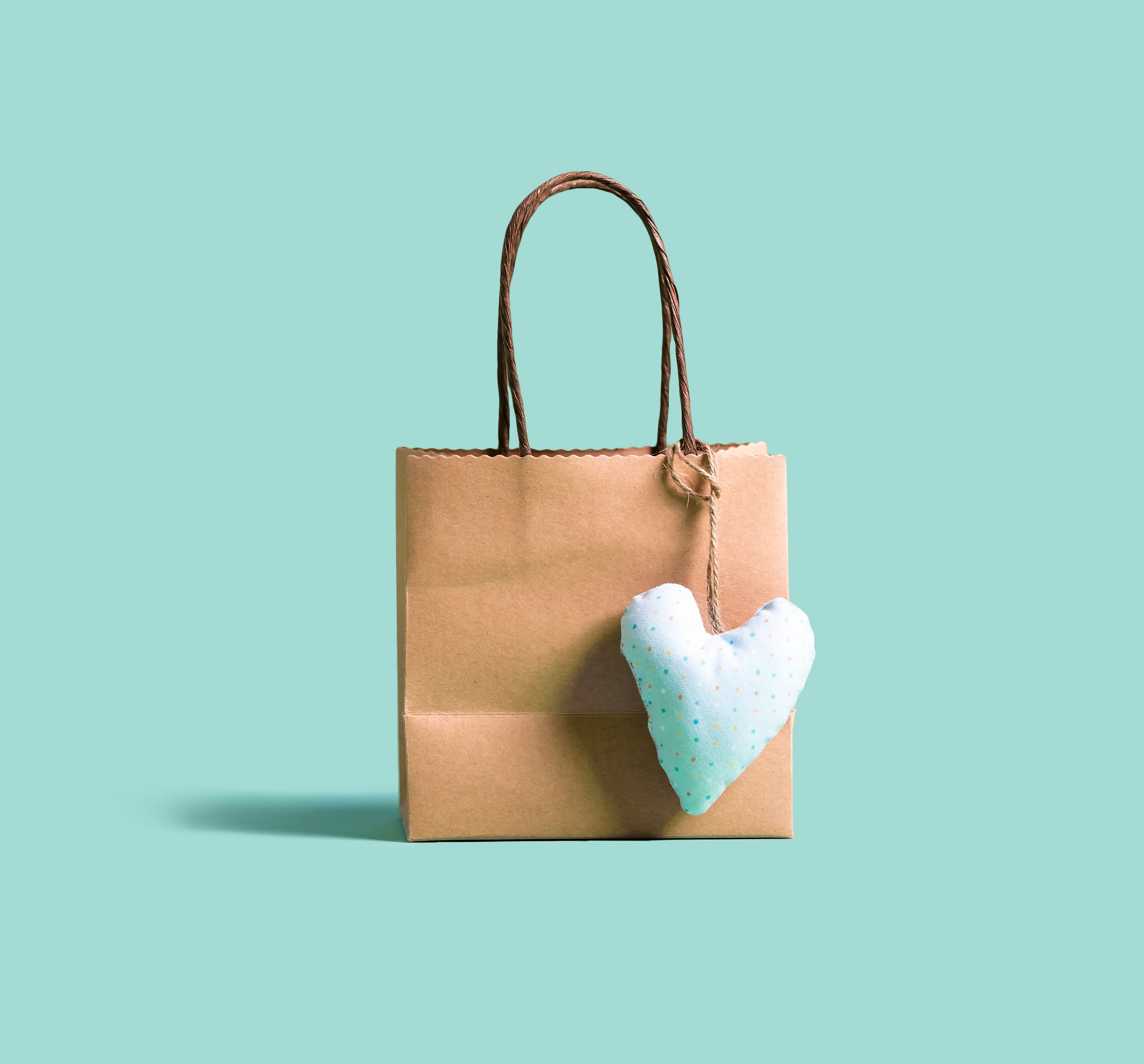 A brown kraft paper shopping bag with small blue felt heart cushion against a matching blue background