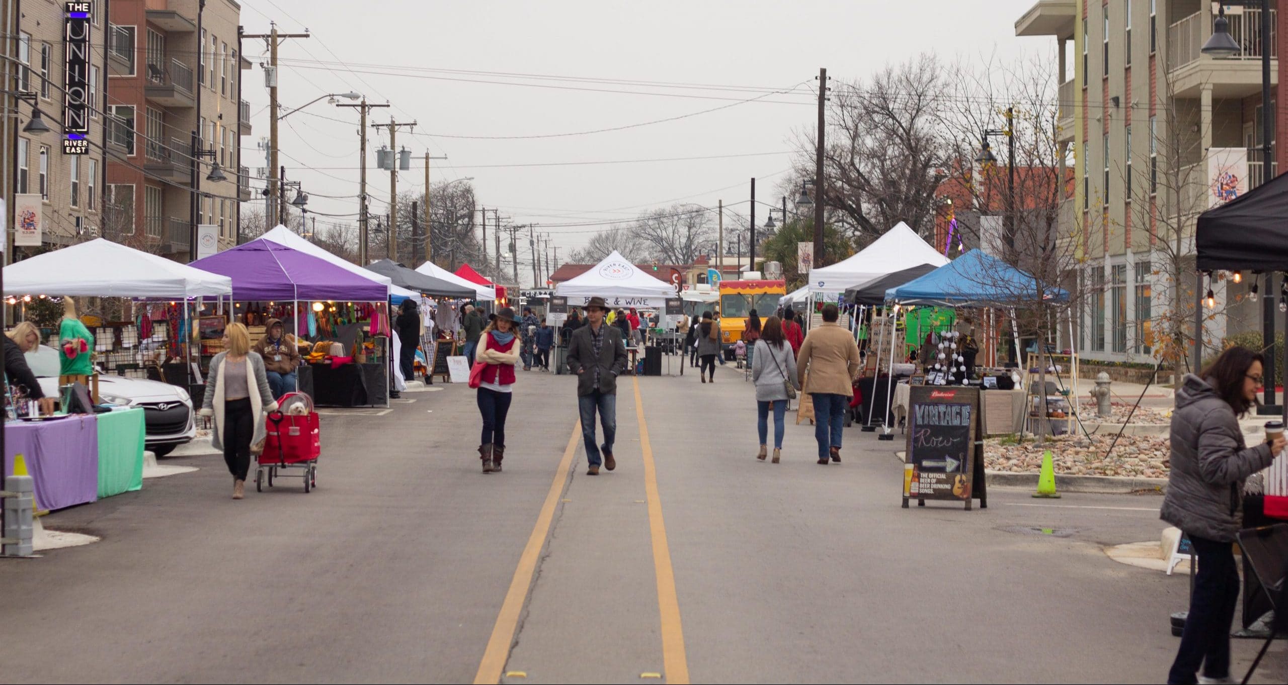 Several people walk down a street lined with canopies at a local arts and crafts show in Fort Worth