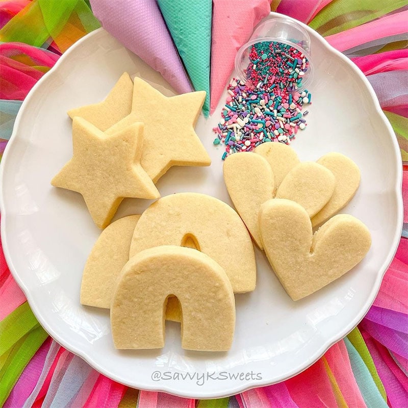 a rainbow background surrounds a plate of naked sugar cookies, icing, and sprinkles by savvy k sweets