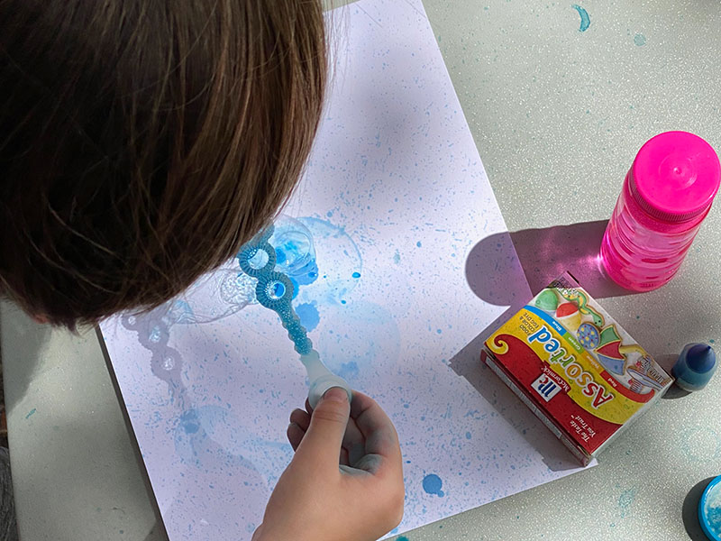 a child blowing bubble art on a blank piece of paper