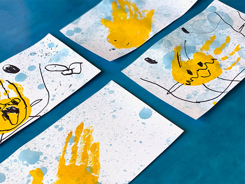 Finished bubble art and drip painted cards with handprints and drawings on them in front of a blue background