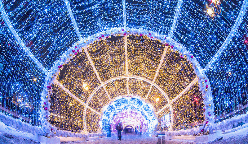 a lighted christmas tunnel features tons of blue and warm yellow lights over a long walking trail