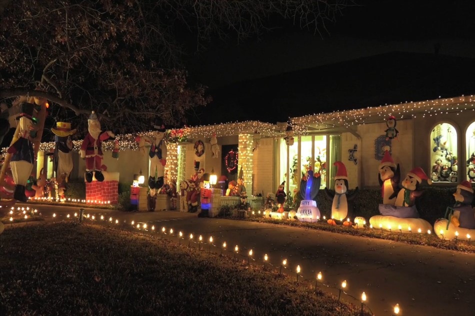 A house is lit up with christmas lights all along their driveway and christmas decor stands alongside