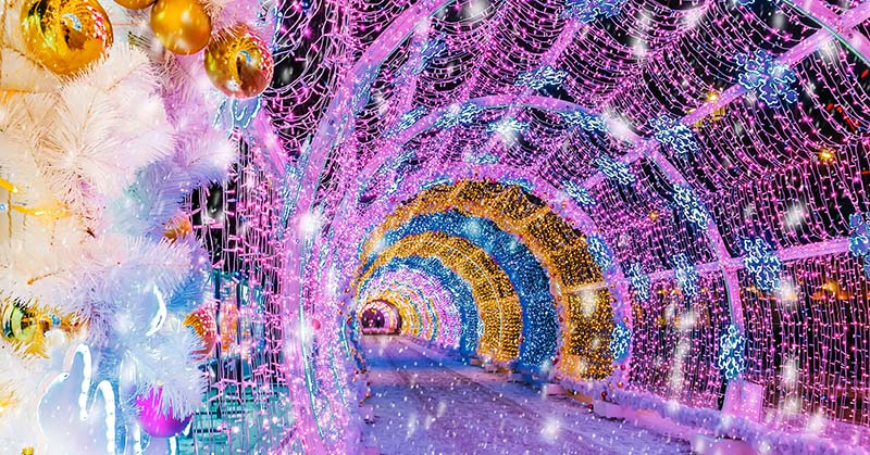 A road surrounded by a tunnel of lights, decorations, and ornaments. 