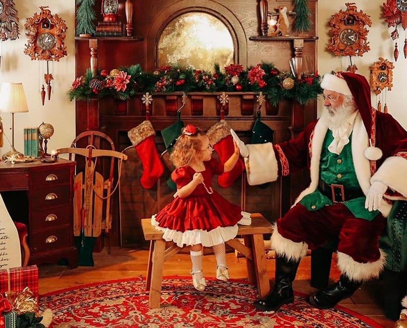 a little girl high fives santa in a cozy den full of christmas decorations