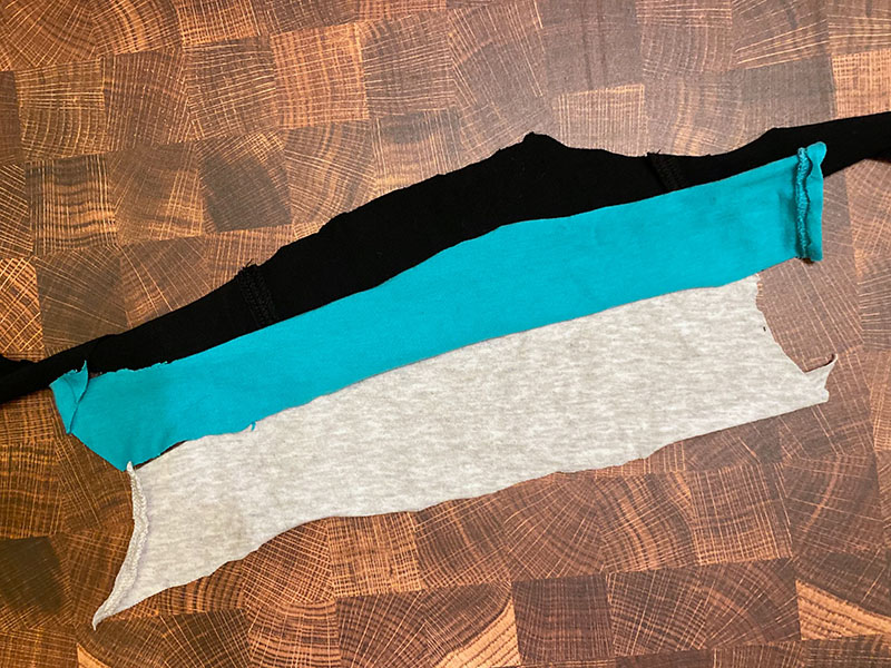 Three strips of knit fabric with varying widths are laid across a wood surface for comparison