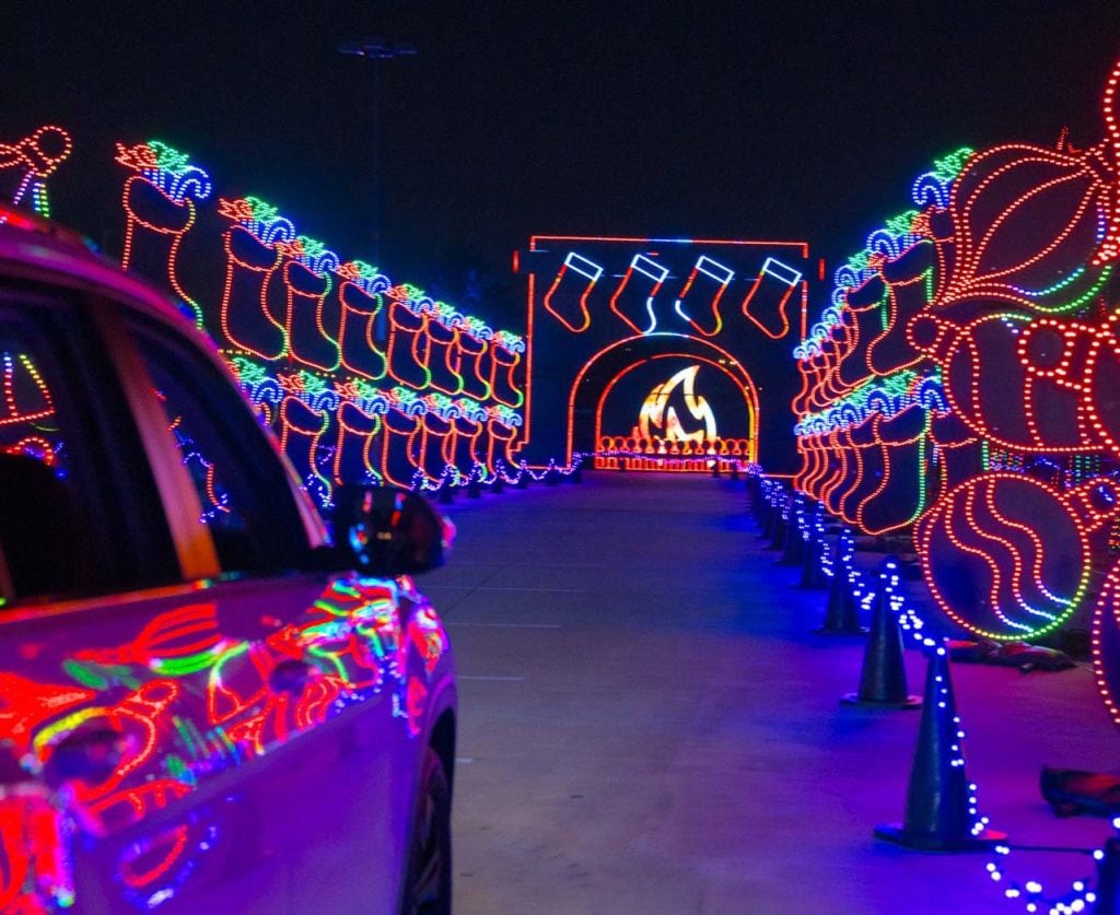 Christmas lights illuminate a white car driving between rows of lights