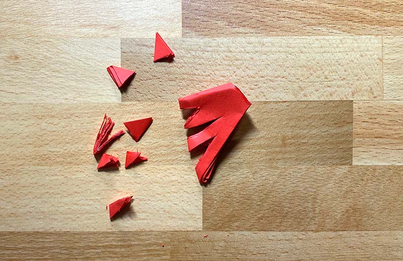 A red piece of paper has been folded several times into a triangle and then cut