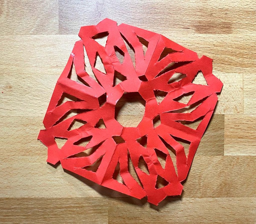 A red paper snowflake has been cut and unfolded to reveal the entire design