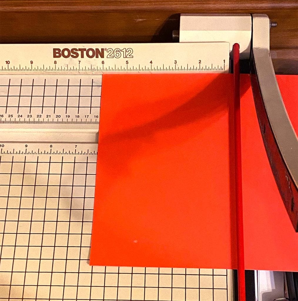 An old school paper guillotine is open to cut a piece of bright red cardstock