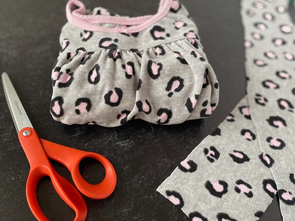 A pair of fleece pajamas is folded neatly next to a pair of orange handled scissors and strips of fabric
