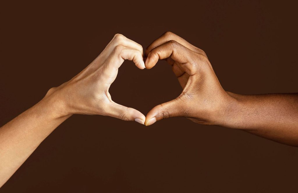 Two people hold their hands together to create one single heart symbol over a brown background
