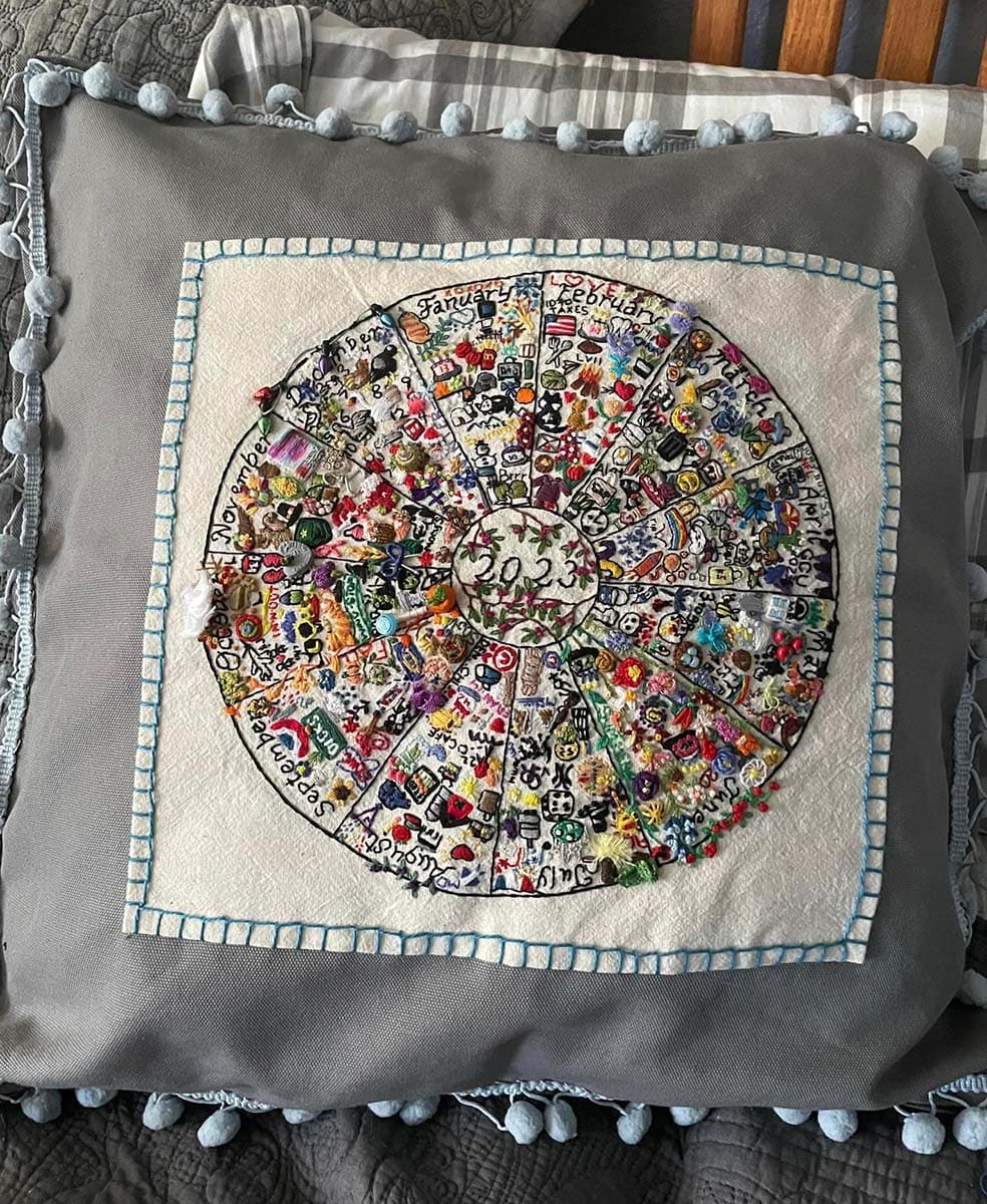 A finished embroidery journal has been stitched onto a fluffy gray pillow