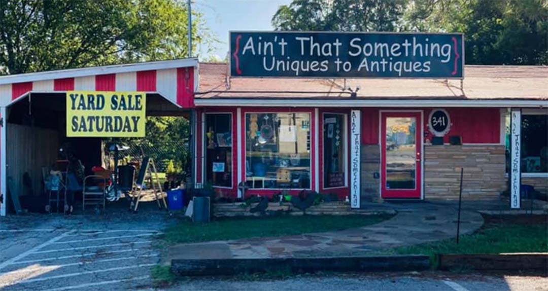 A red building with a large black sign with white text that reads "ain't that something uniques to anitiques"