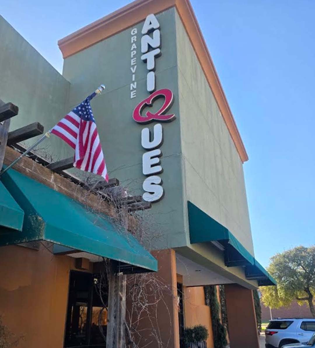 The two story biege and tan building with white sign that reads "Grapevine Antiques" against a blue sky