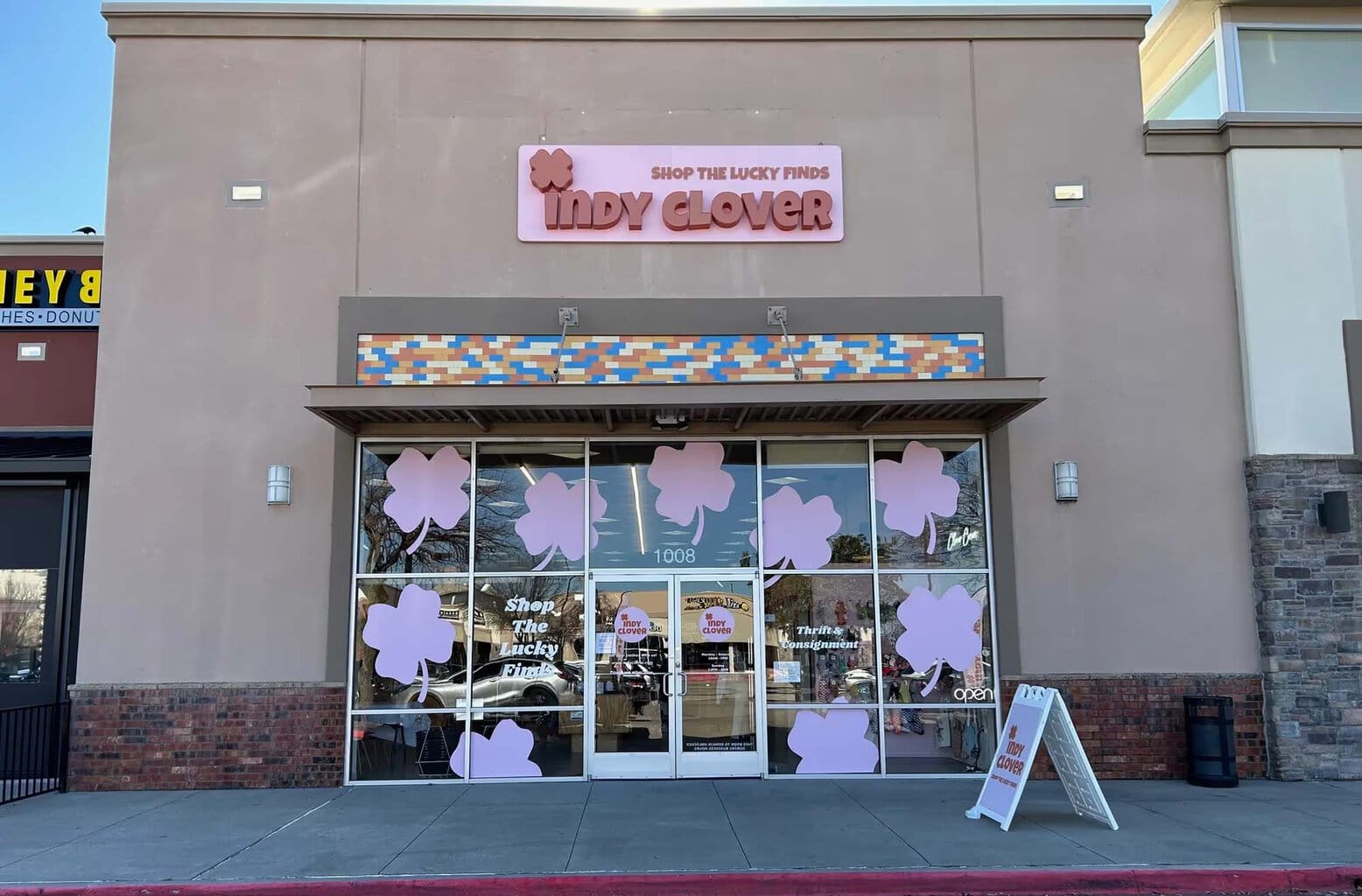 A biege brick building with colorful flowers on the awning and glass windows.  Banner sign reads "Indy Clover"