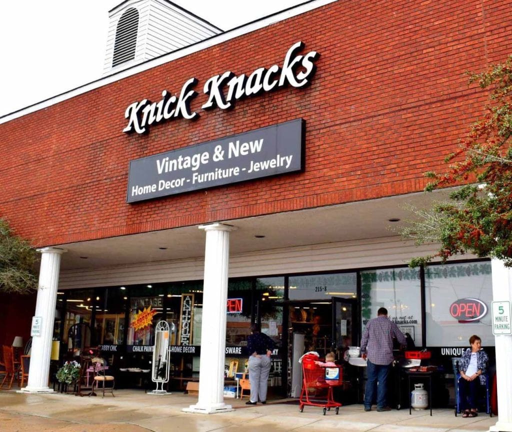 Building with red brick and white pillars with many items on display both on the sidewalk and in store.  Sign reads "Knick Knacks"