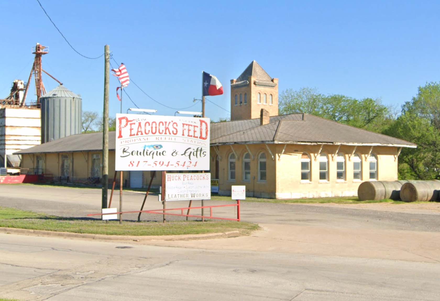 A unique building with a small steeple has a large white sign out front that reads Peacock's Feed & Boutique & Gifts