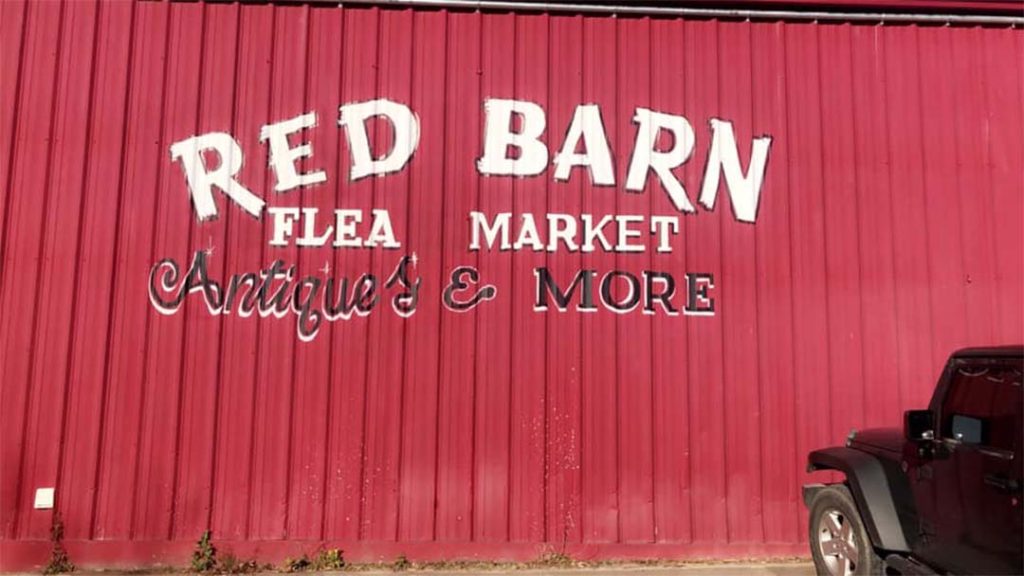 The side of a large metal barn is painted red with the white letters that read "red barn flea market antiques & more"