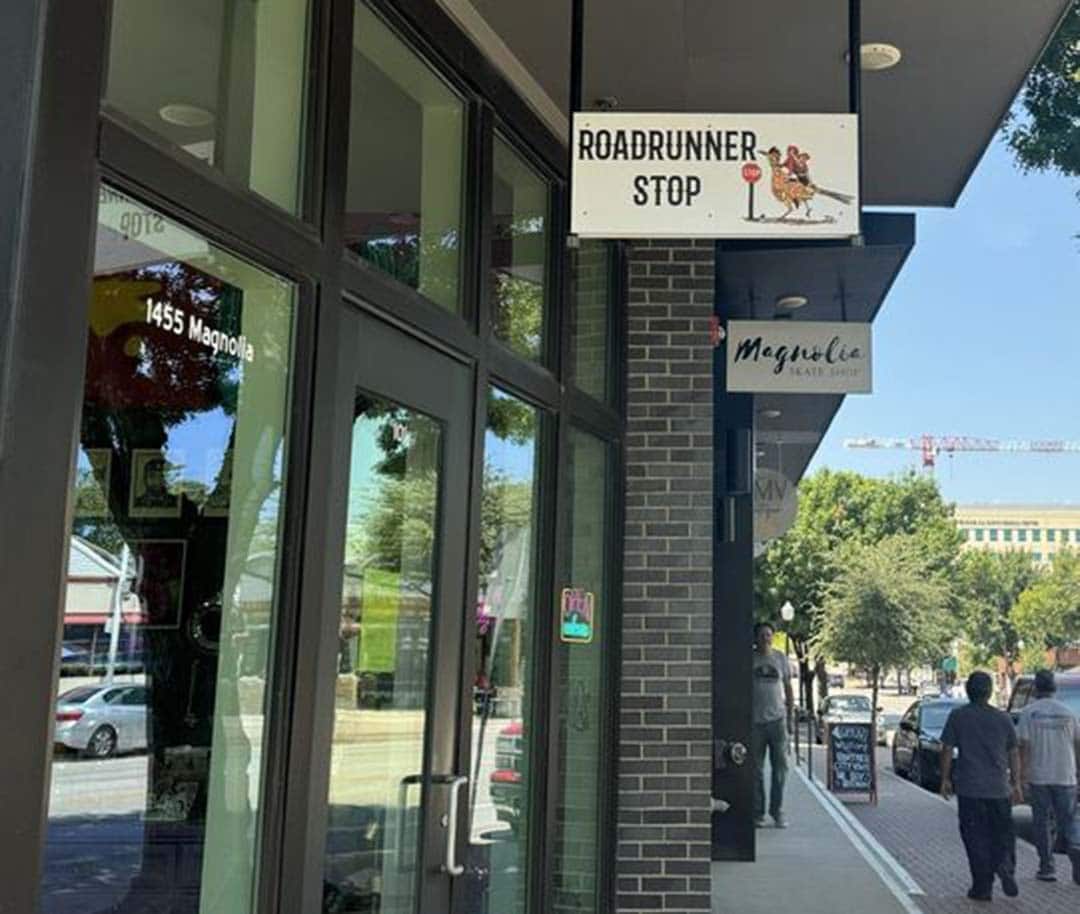 A brick and glass storefront with a white hanging sign that reads "Roadrunner Stop"