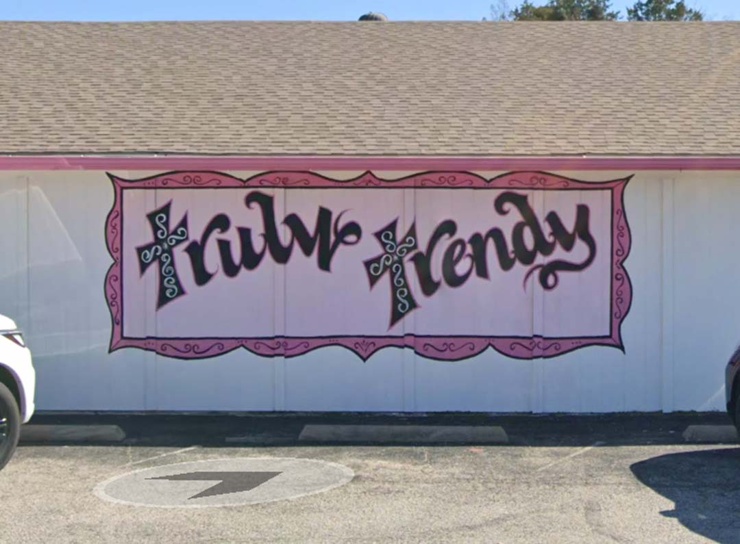 a white building with beige roof and pink trim.  Mural on the wall is framed text "truly trendy"