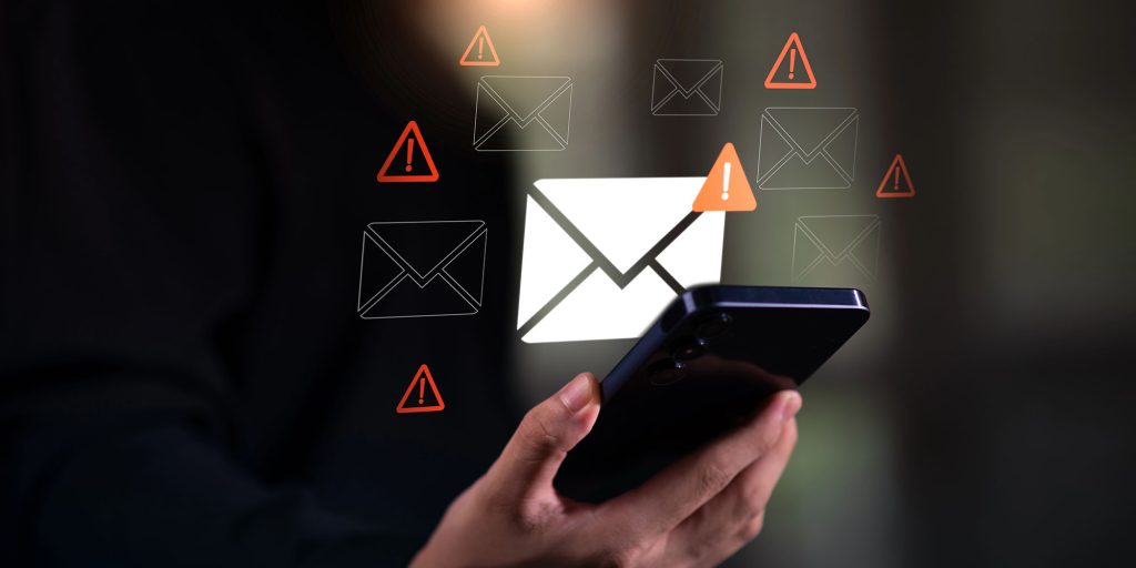 close up of a hand holding a cellphone with an email icon hovering above it. Images of warning symbols surround the phone.