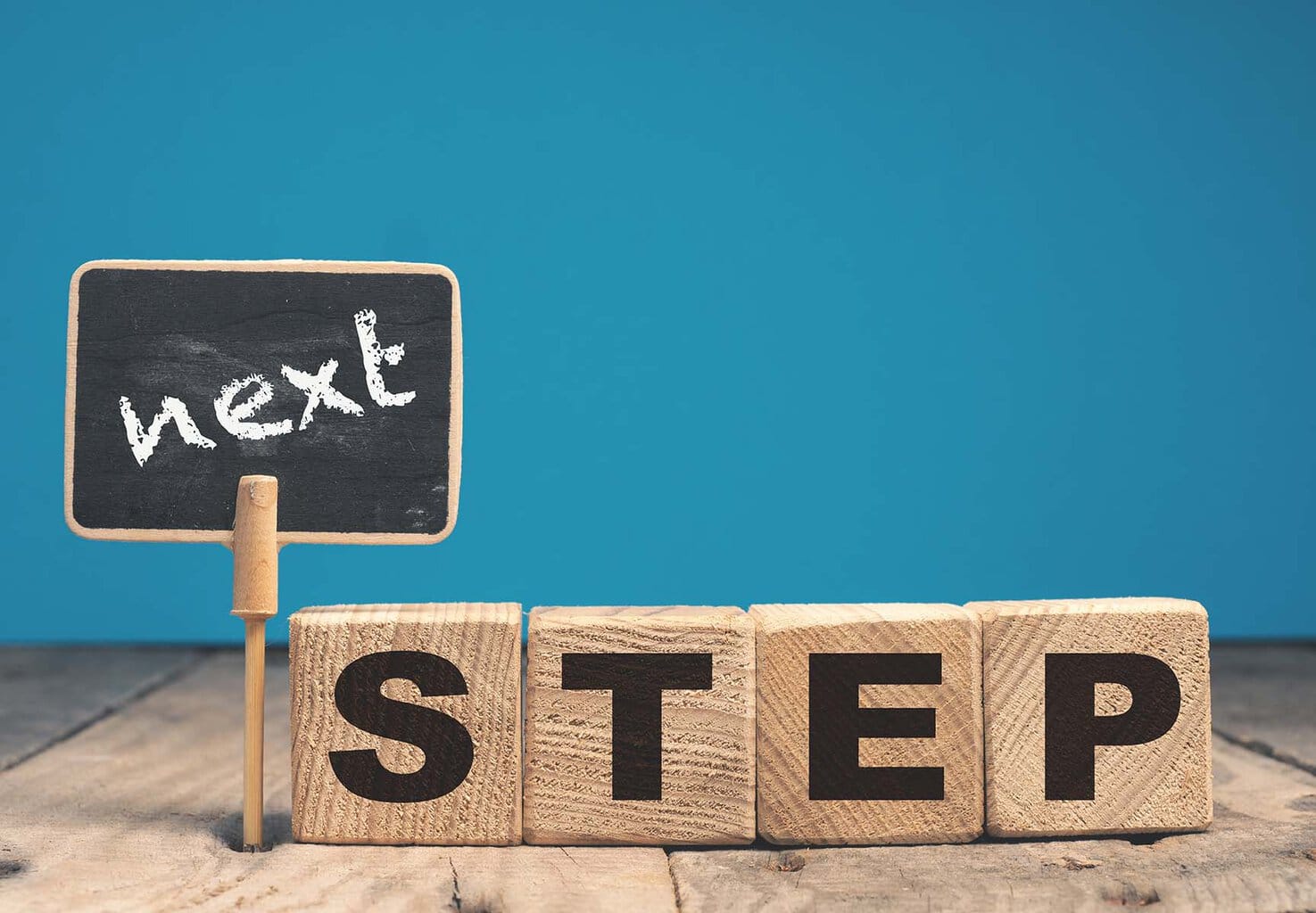 A blue background with a small sign and blocks in front that combined read "next step"